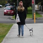 Frau geht mit ihrem kleinen Hund an der Leine über einen Gehweg
